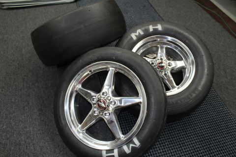 2003 Ford Crown Victoria - Two M&H drag slicks mounted on polished five-spoke aluminum wheels with a bare slick behind on a gray checkered shop floor.