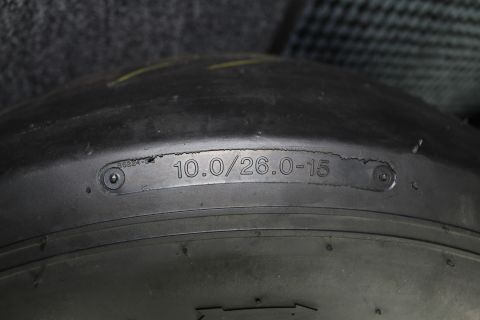 2003 Ford Crown Victoria - Close-up of a slick tire sidewall metal plate stamped 10.0/26.0-15 resting on a gray checkered shop floor.