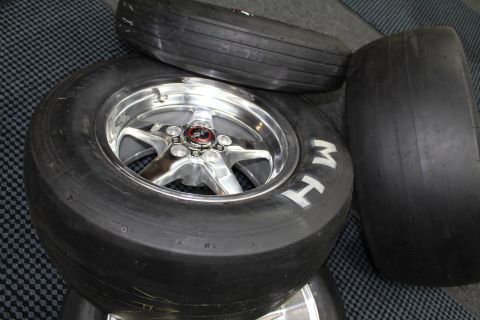 2003 Ford Crown Victoria - M&H slick tires on polished five-spoke aluminum drag wheels, one with a red center-cap emblem, grouped on a checkered floor.