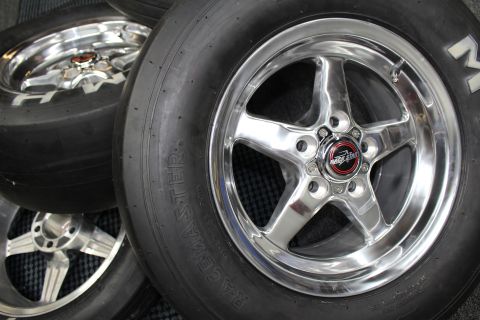 2003 Ford Crown Victoria - polished five-spoke aluminum drag wheel mounted on a Racemaster slick sits beside other wheels on a checkered mat.