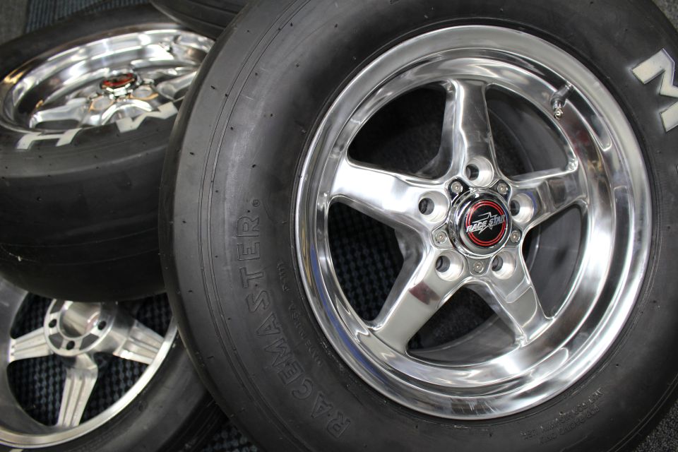 Polished five-spoke drag wheels mounted on slick tires resting on a mat