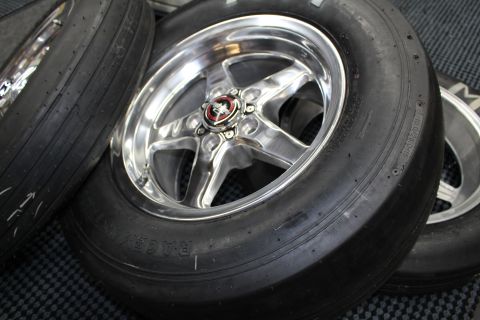 2003 Ford Crown Victoria - polished five-spoke drag wheel with a red center cap sits on a slick tire among several wheels on a mat.