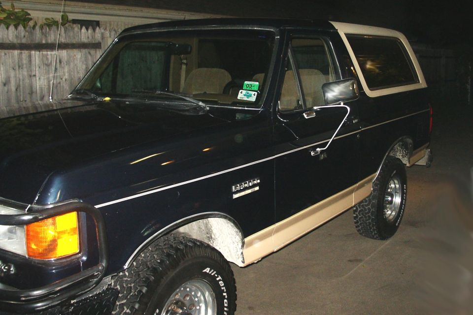 Dark blue and tan Ford Bronco Eddie Bauer at night with brush guard and chrome wheels