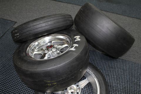 2003 Ford Crown Victoria - Several drag slick tires on polished aluminum wheels are stacked together on a checkered floor mat.