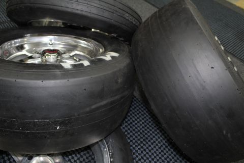 2003 Ford Crown Victoria - Stacked drag slick tires on polished aluminum wheels rest together on a dark checkered floor mat.
