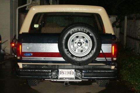 1991 Ford Bronco - Rear view of a 1991 Ford Bronco with a spare tire mounted and a distinctive red, white, and blue stripe.