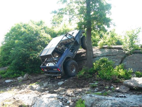 1988 Ford Bronco - Modified 1988 Ford Bronco navigating a steep, rocky trail and leaning against a tree.