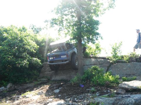 1988 Ford Bronco - A blue Ford Bronco is navigating a rocky trail, with its rear end facing the camera.