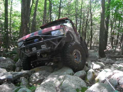 1988 Ford Bronco - Modified Ford Bronco navigates a rocky trail through a dense forest.