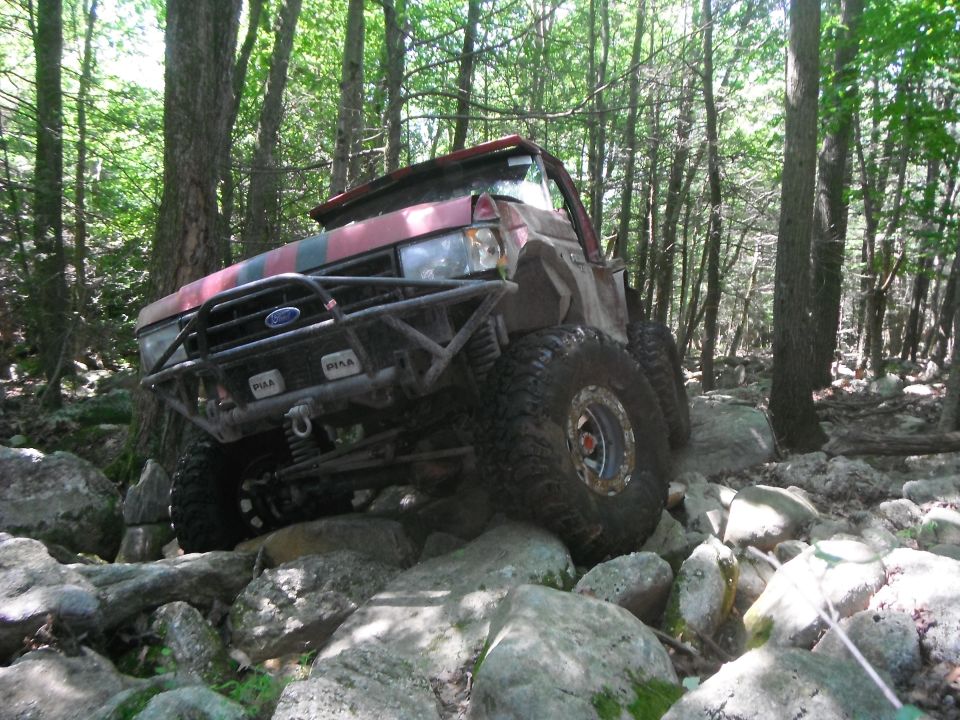 Red and black Ford Bronco off-roading over rocks in a forest