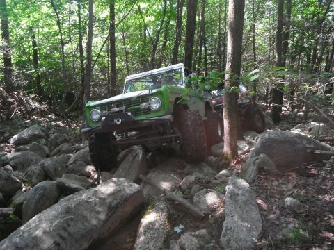 1988 Ford Bronco - This first-generation Ford Bronco navigates a challenging rocky path through a wooded area.
