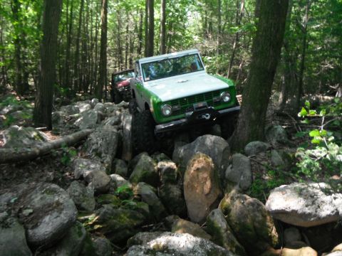 1988 Ford Bronco - Two 4x4s tackle a challenging rocky path through a dense forest.