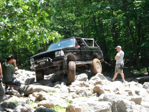 1988 Ford Bronco - A black Ford Bronco navigates a rocky off-road trail with trees in the background.