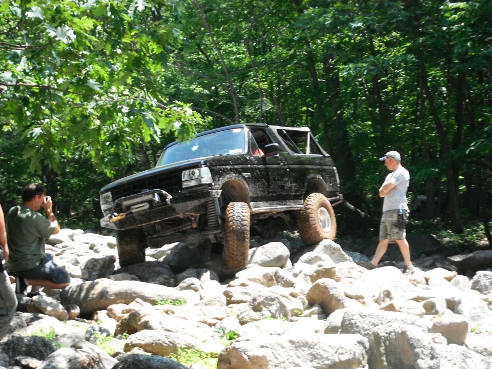 Black Ford Bronco climbing over rocks on a trail. A person is taking a photo of it