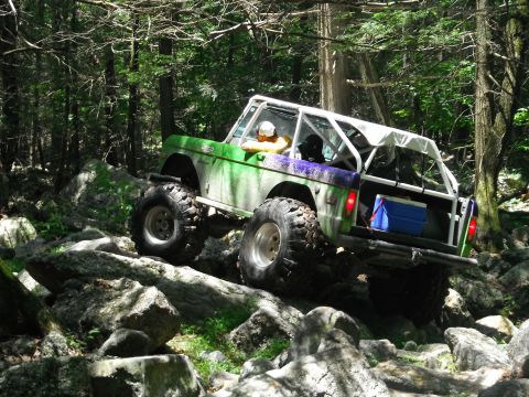 1988 Ford Bronco - This modified Ford Bronco is tackling a challenging rocky terrain in a wooded area.