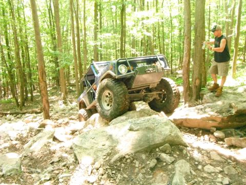 1988 Ford Bronco - A modified off-road vehicle navigates a rocky trail through a dense forest.