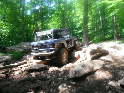 1988 Ford Bronco - A modified Ford Bronco navigates a rocky path through a dense forest.