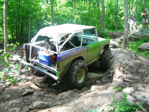 1988 Ford Bronco - This modified Bronco navigates a challenging rocky terrain in a wooded area.