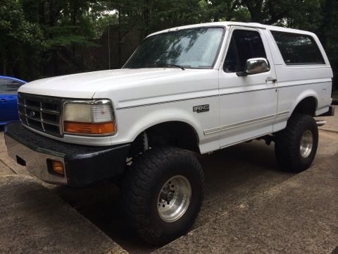 1994 Ford Bronco - This lifted white Ford Bronco is shown from a three-quarter front angle, highlighting its off-road tires and suspension.
