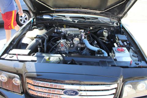 2003 Ford Crown Victoria - engine bay of a black Ford sedan reveals a supercharged engine viewed over the front Ford-badged grille.