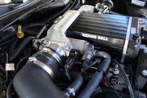2003 Ford Crown Victoria - Close-up of a Kenne Bell supercharger's finned top and throttle body, with a black intake hose, clamps and wiring in the engine bay.