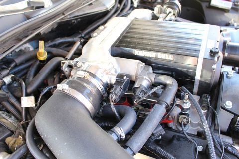 2003 Ford Crown Victoria - Engine detail of a Kenne Bell supercharger feeding a throttle body, with a clamped black intake hose and red engine accents below.