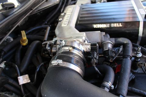 2003 Ford Crown Victoria - Close detail of a Kenne Bell supercharger and throttle body joined to a clamped black intake elbow in the engine compartment.
