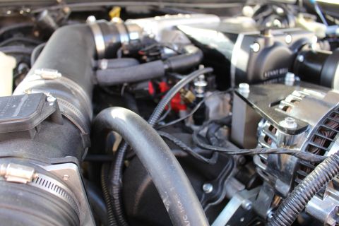 2003 Ford Crown Victoria - Cluttered engine-bay detail showing a clamped intake tube, looped vacuum hoses, alternator and the edge of a Kenne Bell supercharger.