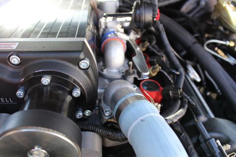 2003 Ford Crown Victoria - Side detail of a Kenne Bell supercharger bearing an oil-warning label, beside a light-blue coolant pipe and red engine-bay accents.