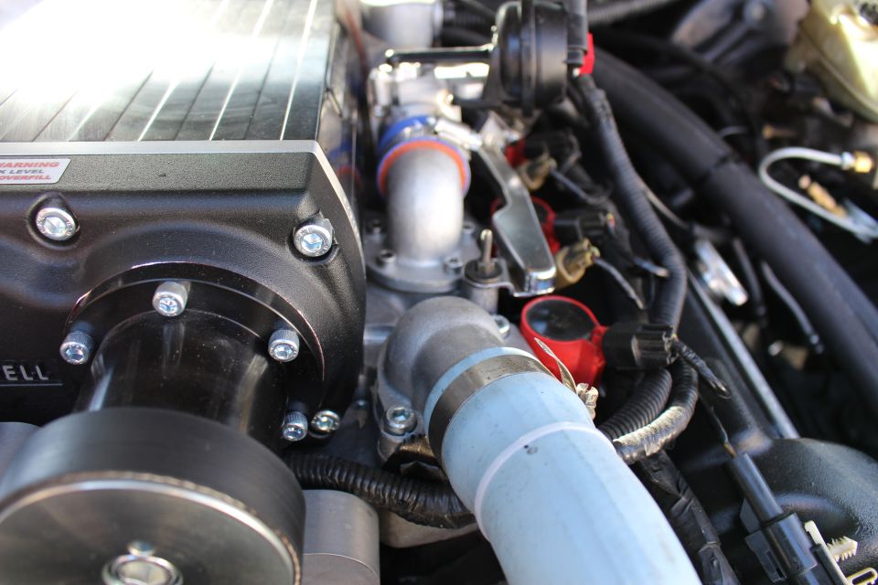 Kenne Bell supercharger side with oil warning label, blue coolant pipe and red caps