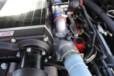 2003 Ford Crown Victoria - Close-up of a Kenne Bell supercharger's labeled side and snout next to a clamped light-blue coolant hose in the engine compartment.