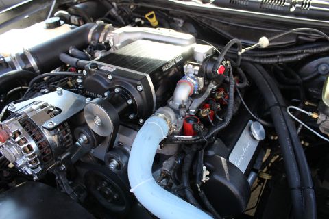 2003 Ford Crown Victoria - Engine bay detail of a Kenne Bell supercharger feeding a light-blue silicone intake elbow next to a chrome alternator and red fuel rails.