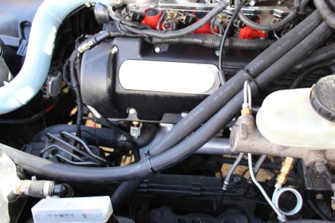 2003 Ford Crown Victoria - Engine bay view of a black valve cover with a blank oval plate next to a translucent brake fluid reservoir and master cylinder.