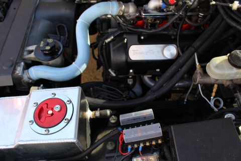 2003 Ford Crown Victoria - Engine bay showing a black Trick Flow valve cover with a blue silicone hose, aluminum tank and red battery disconnect plus fuse block.