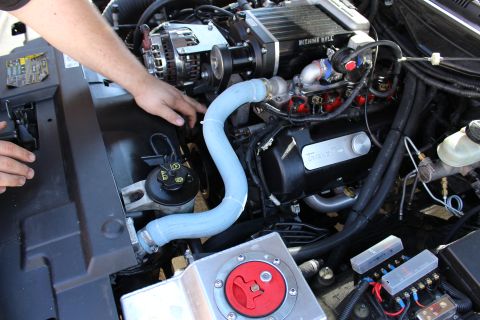 2003 Ford Crown Victoria - hand reaches into an engine bay with a Kenne Bell supercharger, blue silicone hose and red battery disconnect on an aluminum tank.