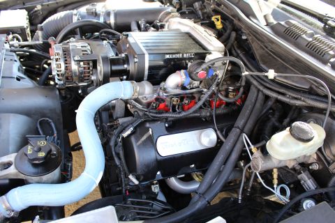 2003 Ford Crown Victoria - Engine bay showing a Kenne Bell supercharger and chrome alternator above a black valve cover marked Mazda with a blue silicone hose.