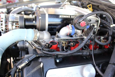 2003 Ford Crown Victoria - Engine bay detail of a Kenne Bell supercharger feeding an aluminum intake elbow over red ignition coils and a wiring harness.