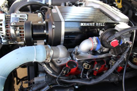 2003 Ford Crown Victoria - Engine bay close-up of a Kenne Bell supercharger joined to a polished aluminum intake elbow above red ignition coils.