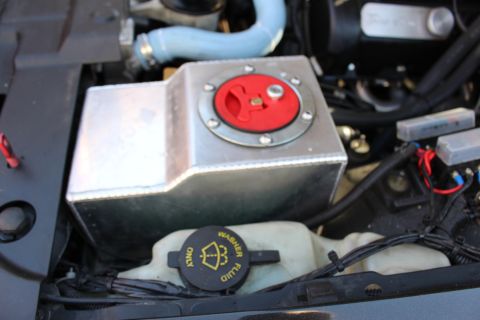 2003 Ford Crown Victoria - Engine bay close-up of a welded aluminum tank topped by a red cap, sitting above a yellow washer-fluid reservoir cap.