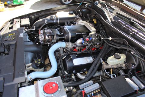 2003 Ford Crown Victoria - Wide engine bay view of a Kenne Bell supercharged motor with a large blue silicone hose, chrome alternator and master cylinder.