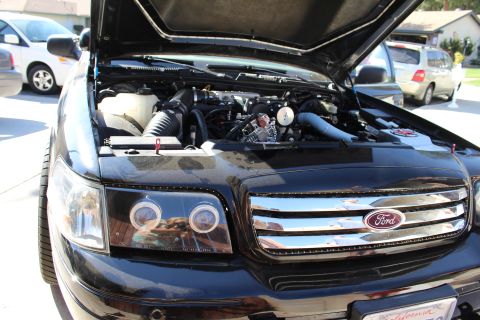 2003 Ford Crown Victoria - black Ford sedan parked outdoors with its hood raised, exposing the engine and showing the chrome Ford grille emblem.