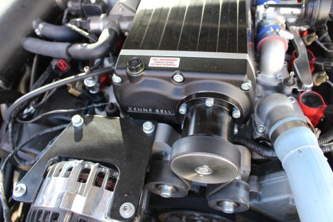 2003 Ford Crown Victoria - Close-up of a Kenne Bell supercharger's black drive pulley and oil warning sticker, with a chrome alternator below and blue hose.