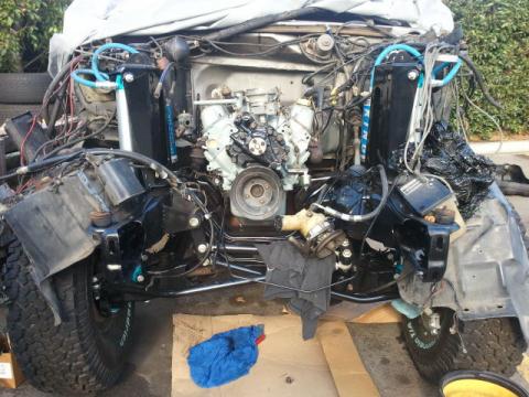 1986 Ford Bronco - The engine bay of a vehicle is exposed, revealing the engine, complex wiring, and front suspension components during a repair or restoratio…