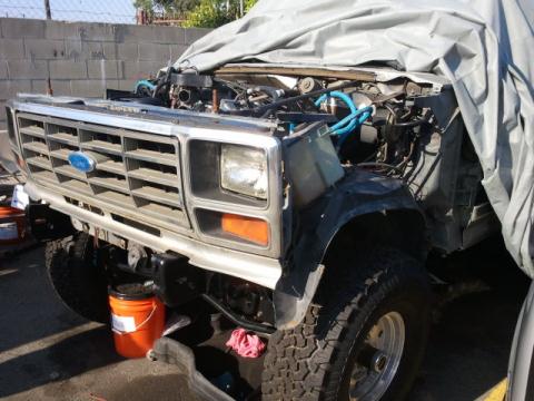 1986 Ford Bronco - A 1986 Ford Bronco is partially covered, revealing its front grille and exposed engine bay.