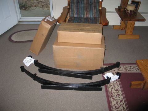 1995 Ford Bronco - Two new leaf springs and boxes of parts are staged on the floor, ready for installation.