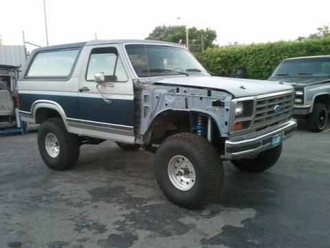 1986 Ford Bronco - This two-tone Ford Bronco is missing its front fenders and hood, revealing its engine bay components and suspension.