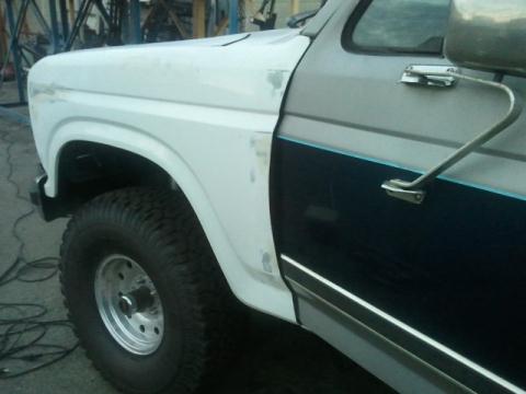 1986 Ford Bronco - The front fender and door of a 1986 Ford Bronco, showing its two-tone paint scheme and chrome accents.