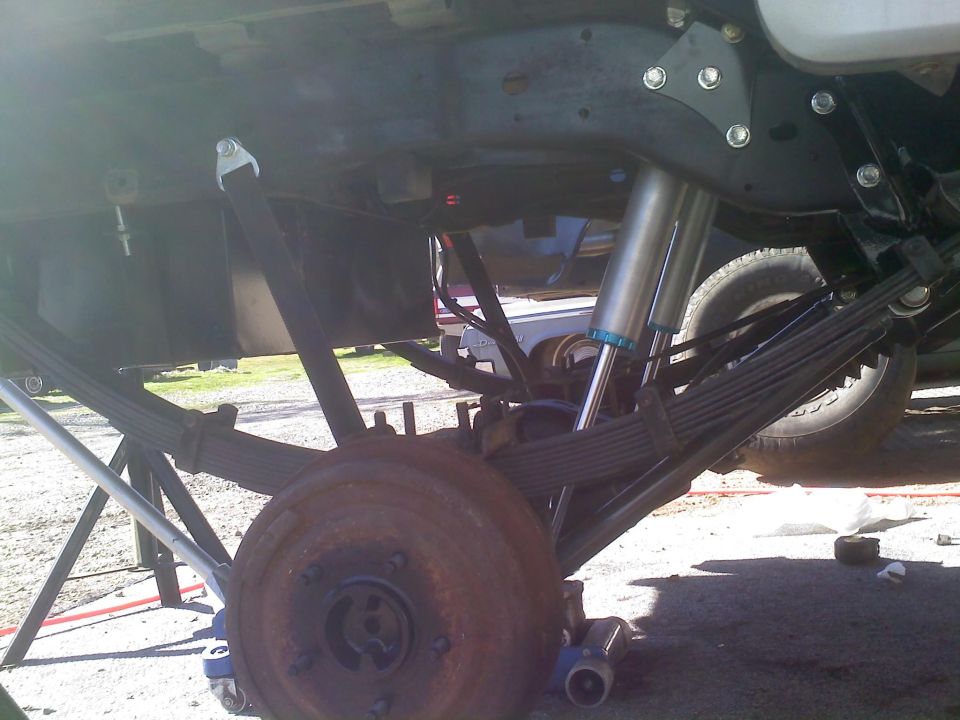 Close-up of a vehicle's rear leaf springs, shock absorber, and drum brake assembly