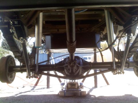 1986 Ford Bronco - The rear suspension and axle assembly of a vehicle are visible from below, supported by jack stands.