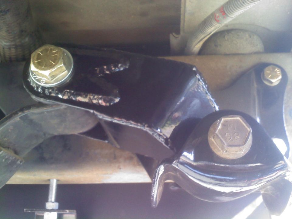 Black painted metal bracket with gold bolts, part of a vehicle's suspension system